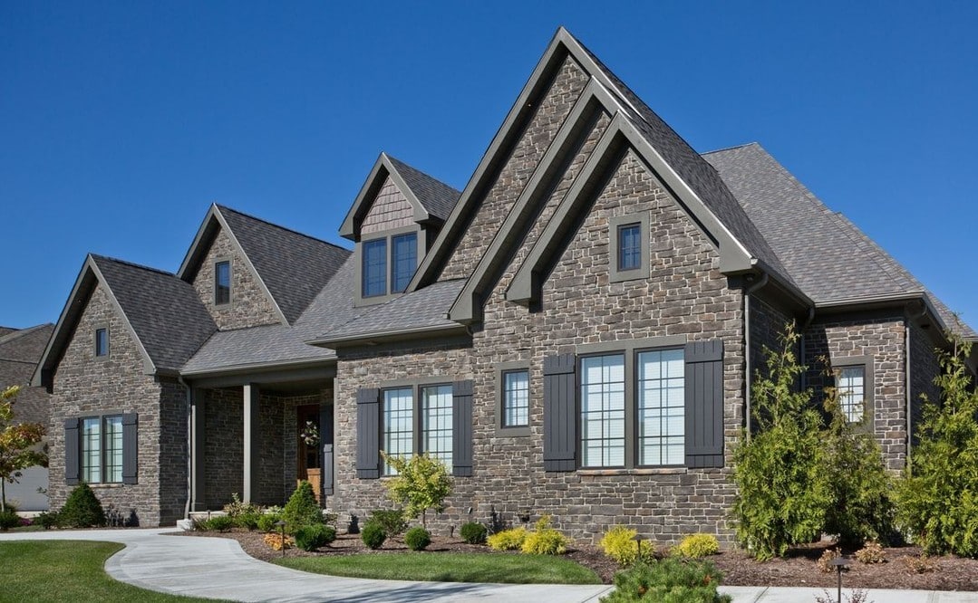 Large home exterior with grey-brown stone veneer, peaked roof, and black shutters