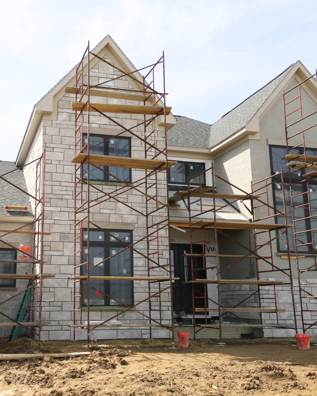 House under construction with light stone veneer and scaffolding on the front exterior