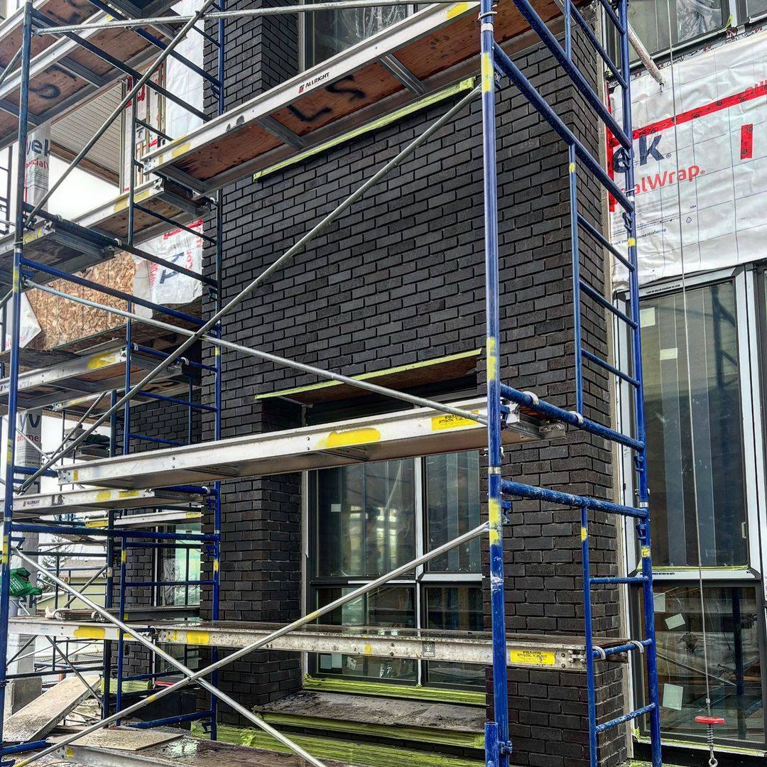 Black brick installation in progress on a modern house exterior with scaffolding in place.